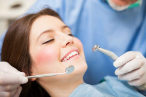 A woman is smiling while being examined by an dentist.