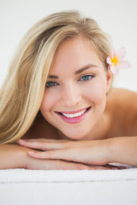 A beautiful blonde woman with blue eyes and pink flower in her hair.