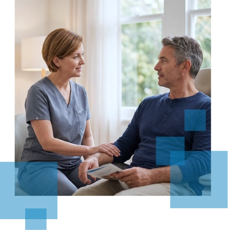 A healthcare professional talks with a patient, seated in a well-lit room with large windows.