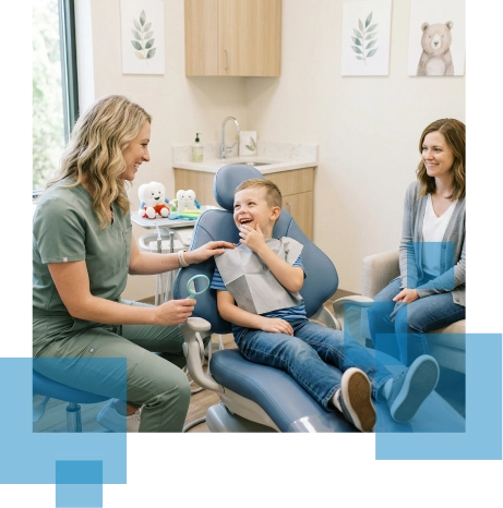 Child laughing in a dental chair with a caregiver and parent in a modern dental office.