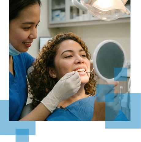 Dentist assisting a patient with dental care while the patient smiles at a mirror.