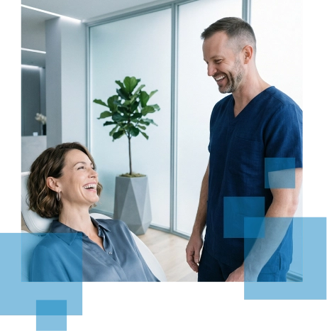 Woman smiling while seated, conversing with a man in scrubs, surrounded by modern decor and greenery.
